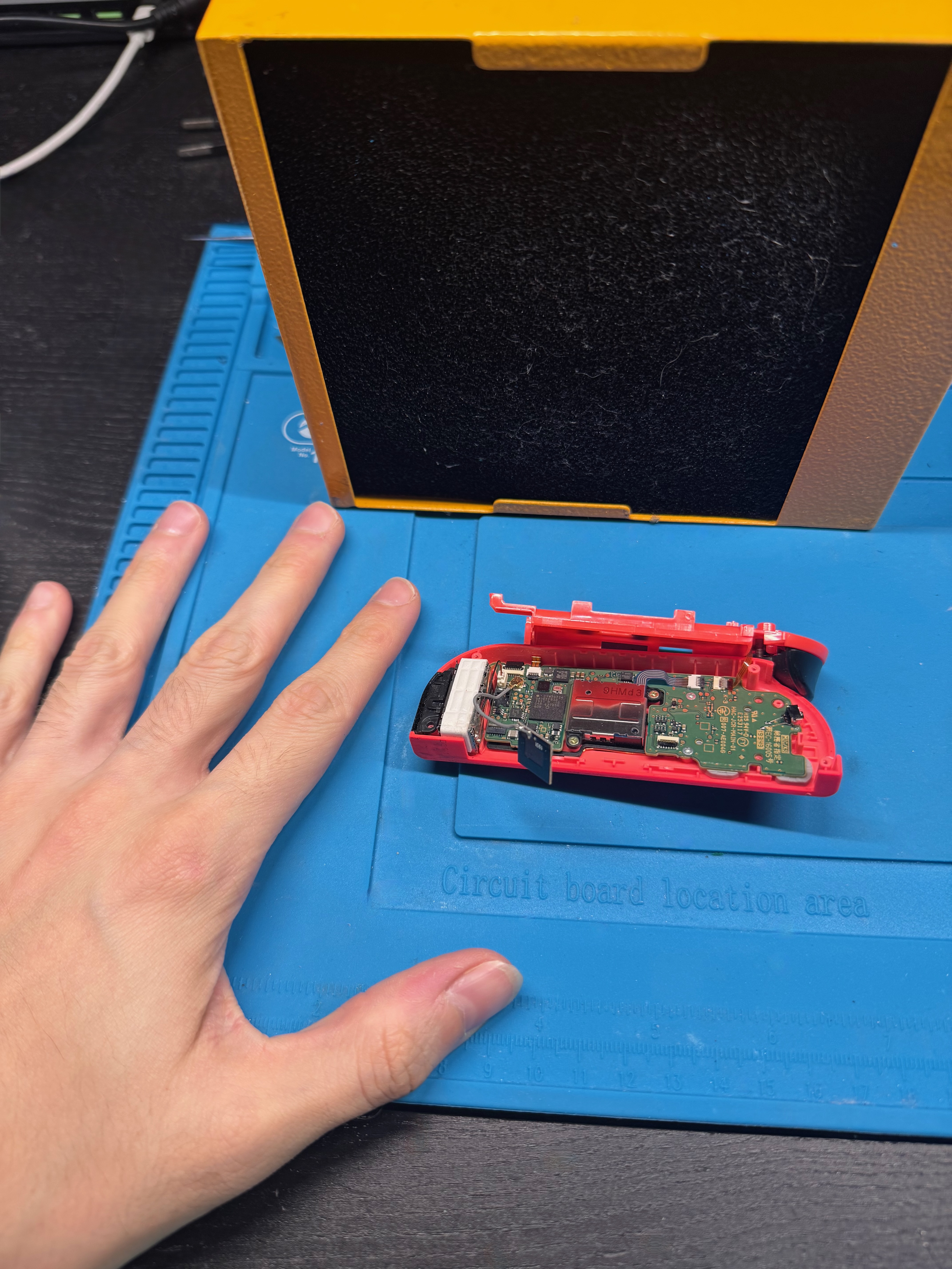 Confronto tra la scheda del Joy-Con e la mano per mostrare le dimensioni ridotte della riparazione
